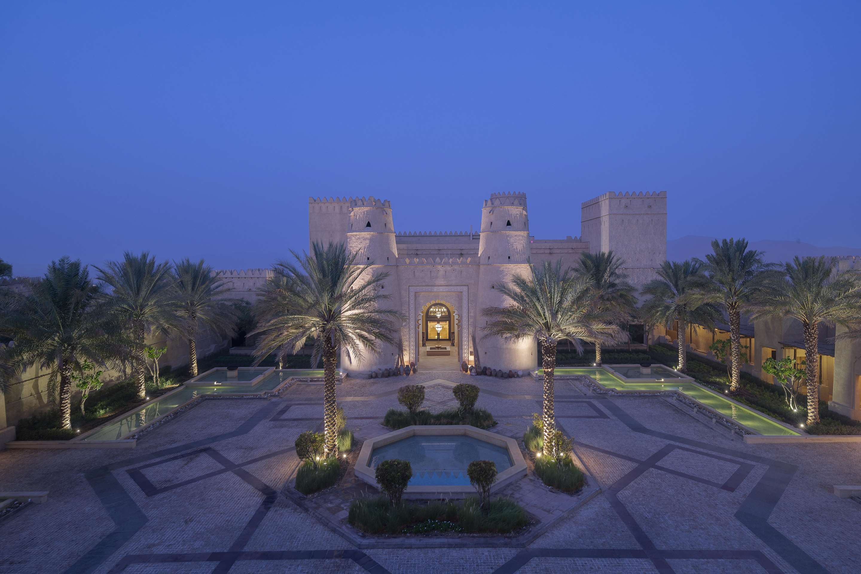Exterior view of hotel entrance with fountain and surrounding garden oasis at twilight